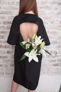 Fashion details, bouquet of white lilies is hidden in the dress of a girl, who is standing backwards