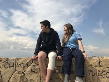 Young couple sitting against sky