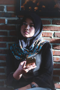 Portrait of young man using mobile phone against brick wall