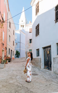Beautiful young woman in white dress standing in alley of picturesque old town.