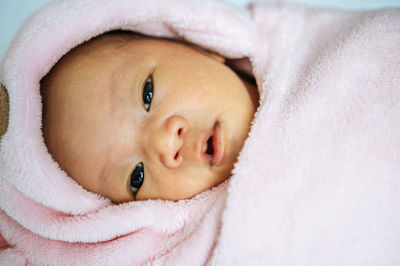 Portrait of baby lying on bed wrapped in blanket at home