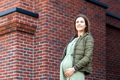 Smiling pregnant woman standing against wall outdoors