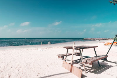 An old wooden table type outdoor bench placed on the white sand beach. background is deep blue 