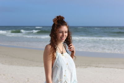 Young woman standing on beach against sky