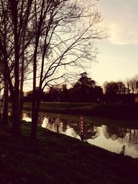 Silhouette bare trees by lake against sky during sunset