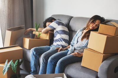 Couple sleeping by cardboard boxes on sofa at home