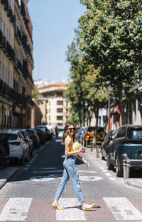 Young stylish woman with drink in hand crossing street