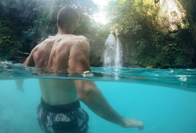 Rear view of shirtless man swimming in pool