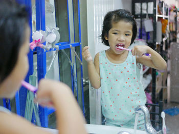 Girl brushing teeth while standing against mirror 