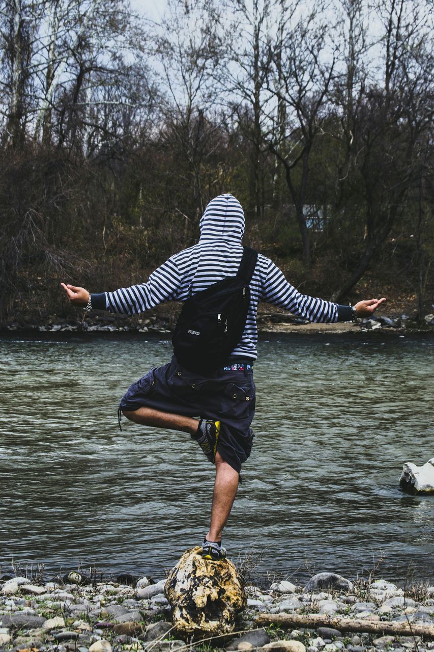 water, tree, full length, lifestyles, leisure activity, river, lake, rippled, standing, rear view, nature, day, waterfront, outdoors, casual clothing, tranquility, person, young adult