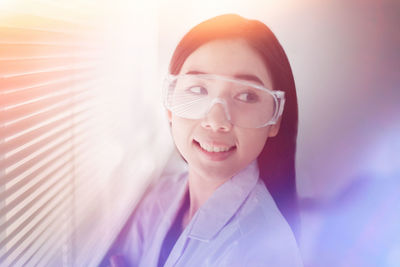 Smiling young woman looking away by blinds