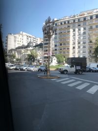 Cars on road by buildings against sky in city