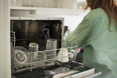 Open dishwasher in kitchen, woman on background