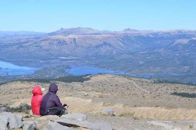 Rear view of people sitting on mountain against sky