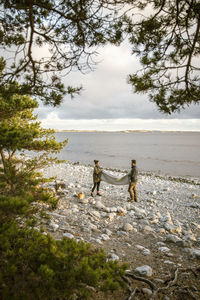 Couple positioning blanket on rocky shore at beach during sunset