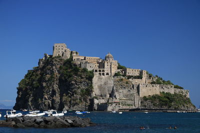 Buildings by sea against clear blue sky