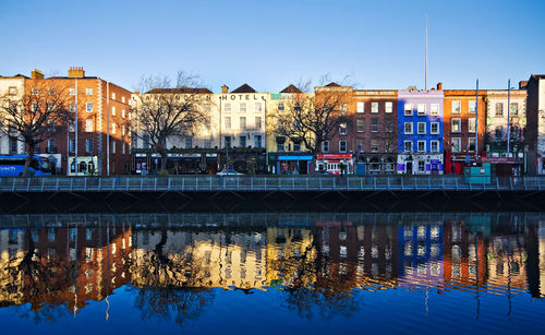 Reflection of buildings in river against clear blue sky