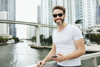 Young man using phone while standing on river in city