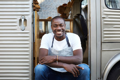 Portrait of smiling mid adult male owner sitting on doorway of food truck