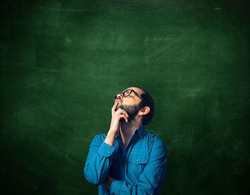 Thoughtful man standing against blackboard