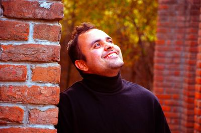 Close-up of smiling young man looking away by wall