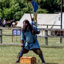 Man with knife and flag standing by container on grassy field