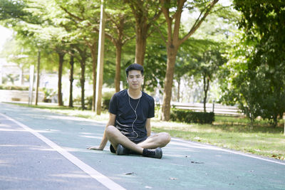 Portrait of young man sitting on plant against trees