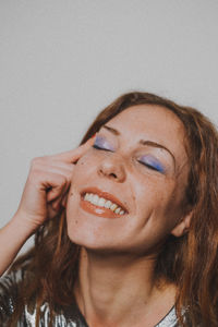 Smiling young woman with eye make-up against wall