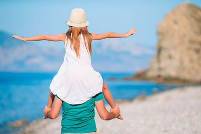 Rear view of father with daughter on shoulder at beach
