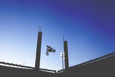 Silhouette biker performing stunt in mid-air at stadium against clear blue sky