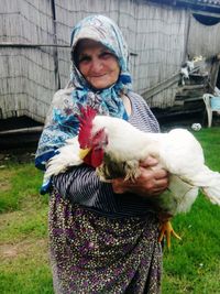 Senior woman carrying hen while standing at farm