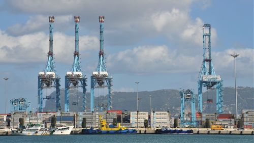 Cranes at harbor against sky