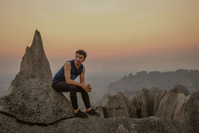 Portrait of woman sitting on rock against sky during sunset