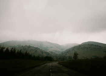 Road leading towards mountains against cloudy sky