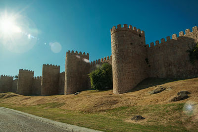 Sunbeam above lined stone towers in the large city wall and green lawn at avila, spain.