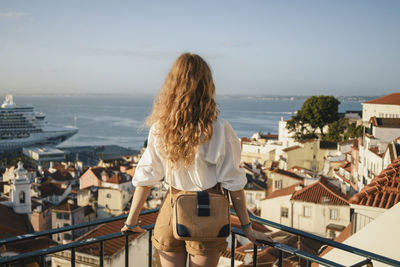 Rear view of woman looking at cityscape against sky