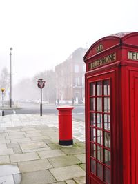 Red telephone booth on street against sky in city