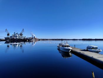 Boats moored in sea against clear blue sky