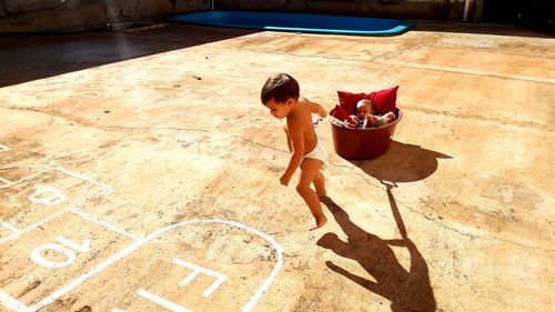 High angle view of shirtless baby boy pulling brother sleeping in bucket