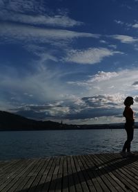 Man standing on pier over lake against sky