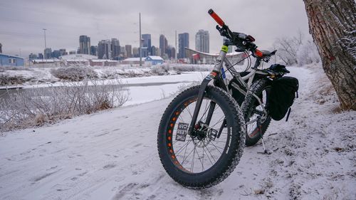 Bicycle on snow covered field by buildings against sky