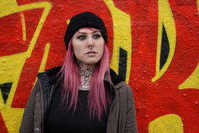 Young woman with pink hair standing against graffiti wall