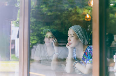 Two woman have coffee together in cafe, view through window glass.