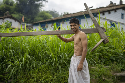 Happy indian farmer standing with wooden plough in rice field