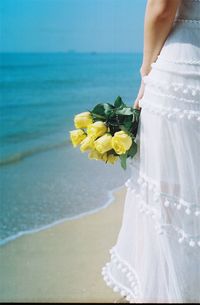 Close-up of woman holding yellow flower on beach