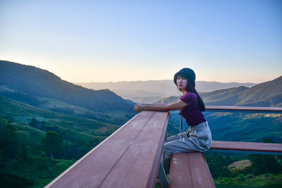 Woman sitting on mountain against sky