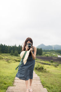 Full length of woman photographing against sky