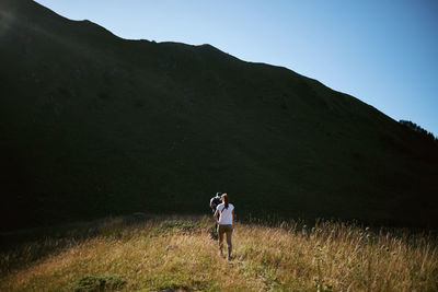 Man and woman walking on field by mountain against sky