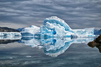 Icebergs reflecting on calm lake against cloudy sky