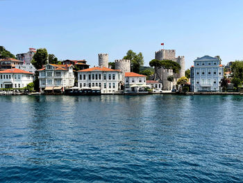 Buildings by river against clear blue sky